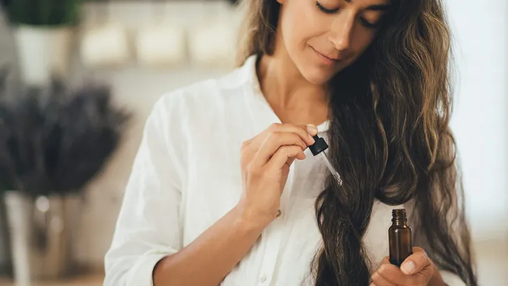 Young woman applying natural organic essential oil on hair and skin. Home spa and beauty rituals.