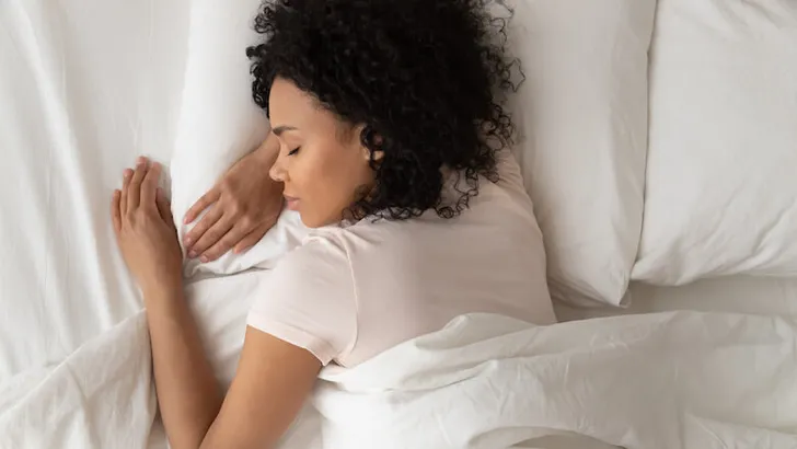 Healthy serene african girl sleeping in comfortable bed, top view