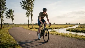 Mannelijke wielrenner in Wieler Revue kleding fietst op een polderweg in Nederland tijdens de gouden uren van een augustusavond.