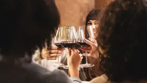 group of happy friends having a dinner and toasting red wine sitting at restaurant table