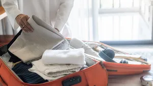 Vrouw pakt kleren en spullen in een open koffer op bed.