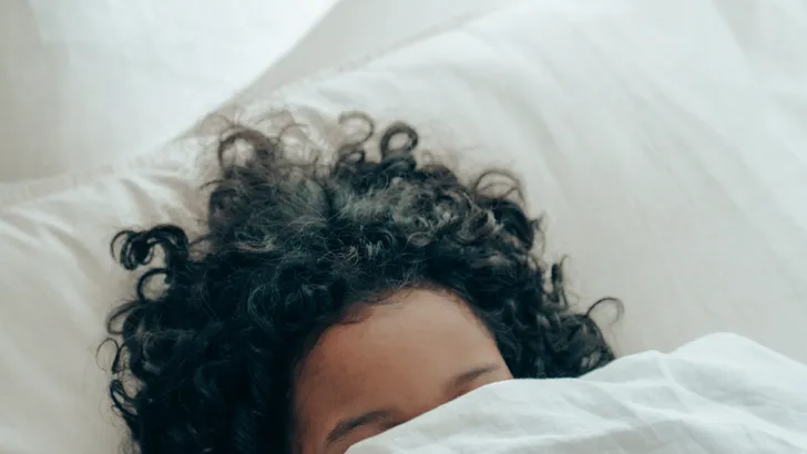Vrouw in bed met hoofd onder de dekens