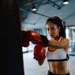 Young Asia lady kickboxing exercise workout punching bag tough female fighter practice boxing in gym fitness class. Sportswoman recreational activity, functional training, healthy lifestyle concept.