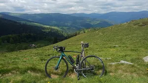 Een Scott racefiets leunt tegen een houten paaltje op de groene flanken van de Petit Ballon, met op de achtergrond een weids uitzicht over de beboste bergen van de Vogezen.