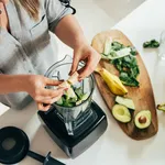 Woman is preparing a healthy detox drink in a blender - a  green smoothie with fresh fruits, green spinach and avocado