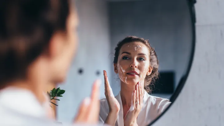 Woman washes in front of the mirror, applying foam to her face