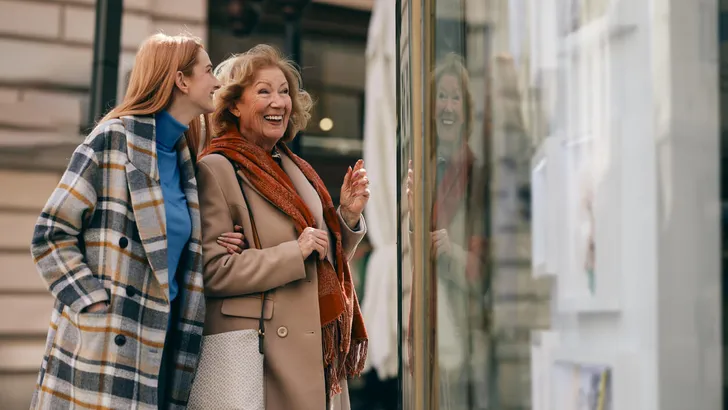 Happy grandmother and granddaughter looking at show window at the gallery.
