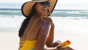 Smiling mixed race woman on beach holiday using sunscreen cream