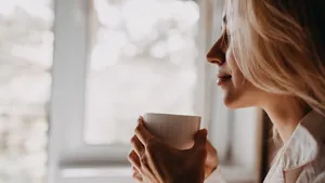 Vrouw met een kop koffie in haar hand, zittend bij het raam in de ochtend.