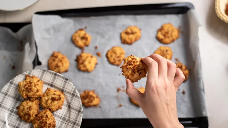 Woman collecting fresh homemade coconut cookies on a plate in the kitchen