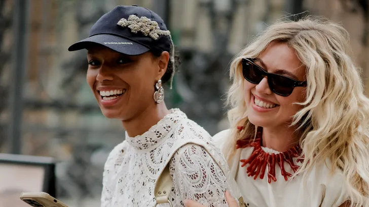 Twee lachende vrouwen tonen hoe accessoires, zoals een pet, grote oorbellen en een statement ketting, hun persoonlijke stijl en outfits versterken.