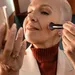 Vrouw met handspiegel doet blush op wangen met kwast