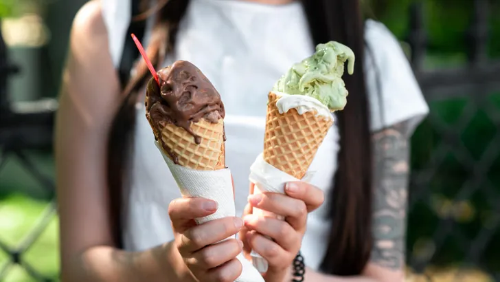 Female hands are holding two melting gelato. chocolate and pistachio flavor in the cones.