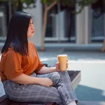 Woman holding her reusable cup and sitting on a street bench