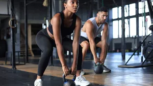 Fit and muscular couple focused on lifting a dumbbell during an exercise class in a gym.