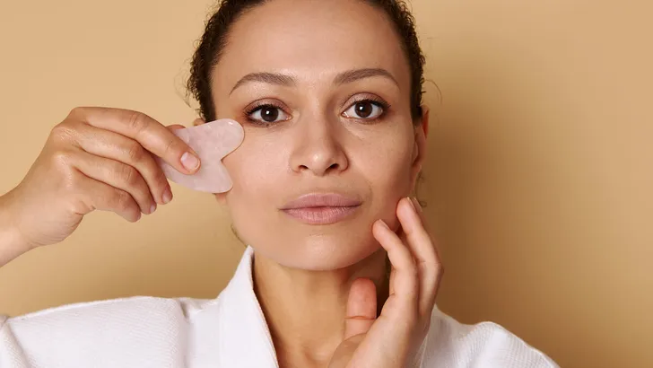 Beauty portrait of mixed race woman using gua-sha for lymphatic drainage facial massage. Spa and skin care concepts. Headshot