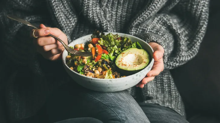 Woman in sweater eating fresh salad, avocado, beans and vegetables