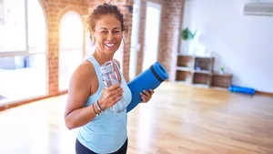 Vrouw met yogamat en fles water in sportzaal