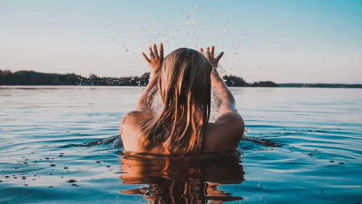 Vrouw zwemt in een meer, nat lang haar.