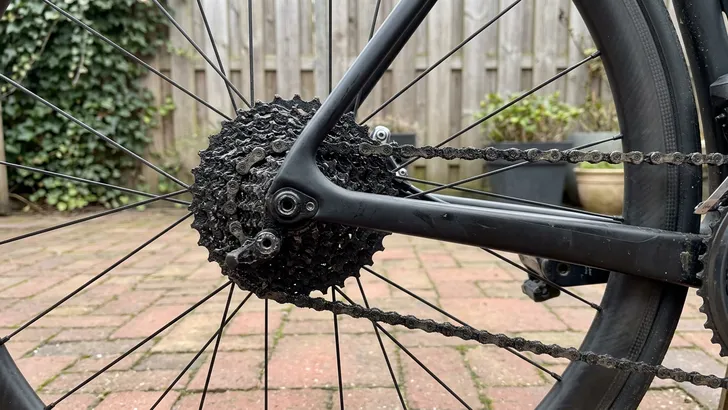 Close-up van een extreem vieze en zwart aangekoekte ketting en cassette op een verder schone carbon racefiets.