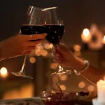 Two young women toasting with wine glasses at dinner table with Christmas lights