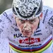 Close-up van Mathieu van der Poel in regenboogtrui, met modder op helm en gezicht, tijdens een cyclocross.
