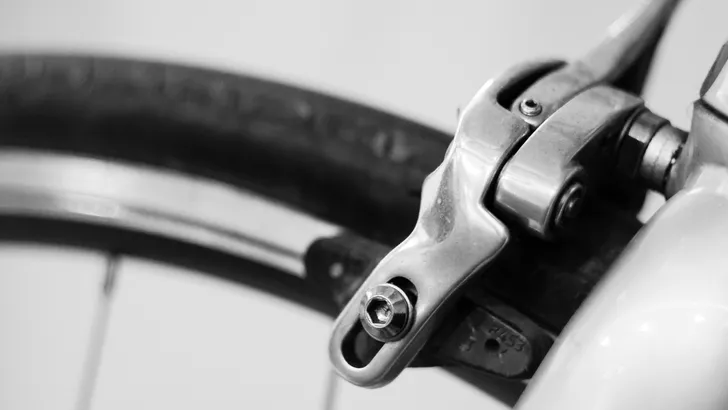 Haarscherpe studio close-up van een klassieke velgrem voor een racefiets, gepresenteerd tegen een donkere achtergrond.