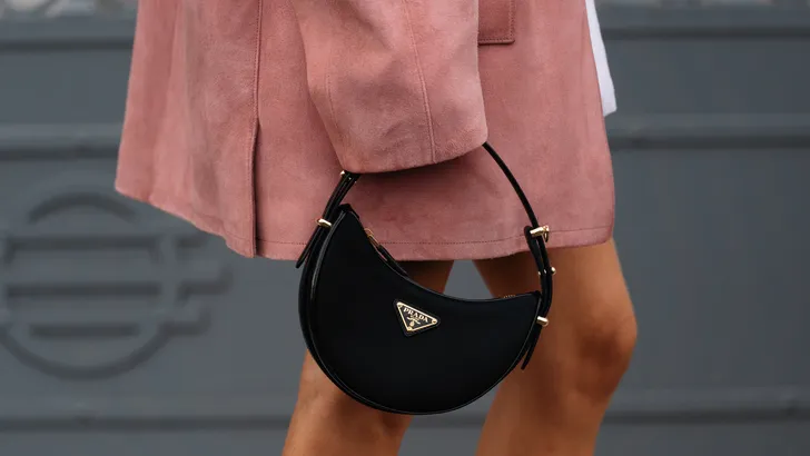 Prada koopt Versace voor ruim een miljard euro.  – Streetstyle-foto van vrouw met roze jas en Prada-handtas