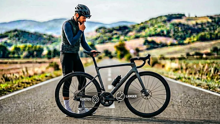 Een mannelijke wielrenner met helm kijkt nadenkend naar het crankstel van zijn racefiets, met een grafische overlay die het dilemma tussen een kortere en langere cranklengte symboliseert.