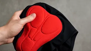 Hand houdt zwarte wielerbroek vast met de zeem binnenstebuiten zichtbaar, rode padding in close-up tegen een neutrale achtergrond