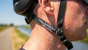 Close-up van een bezwete fietser waarbij de opgedroogde, witte zoutkristallen duidelijk zichtbaar zijn op het zwarte bandje van de helm.