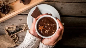 Girl drinks hot chocolate mug, with christmas present on rustic table with blanket or plaid from above, cozy and tasty breakfast or snack. Hands in picture, top view