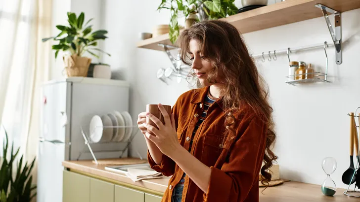 vrouw staat met een kopje thee in de keuken