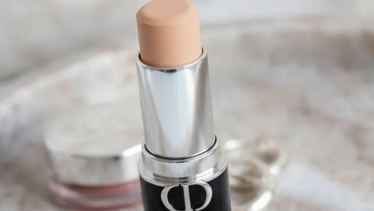 De Dior foundation stick op make-uptafel met andere cosmetica en oorbellen onscherp op de achtergrond.
