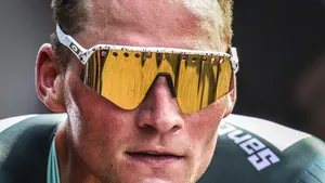 Close-up van het bezwete en geconcentreerde gezicht van Mathieu van der Poel met een gouden spiegelende fietsbril