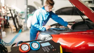 Monteur controleert de airco van een rode auto met een servicemachine