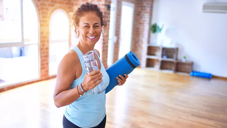 Vrouw met yogamat en fles water in sportzaal
