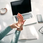 Woman with hand, joint, arm and finger pain, stretching and massaging during work on a laptop.