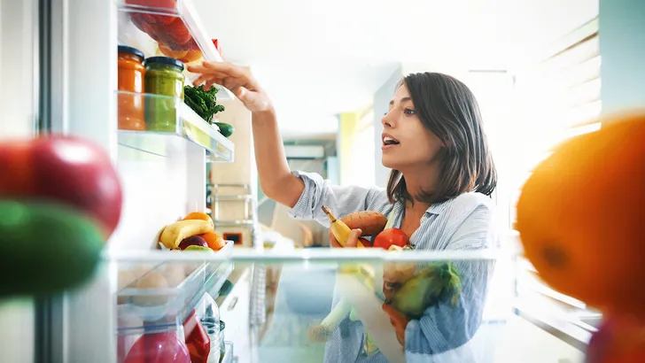 Woman picking up some fruits and veggies from the fridge
