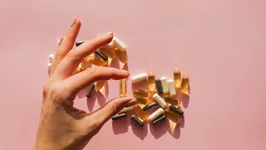 Woman's hand holding a pill or dietic supplement capsule on the pink background