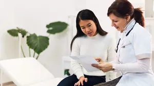 A careful female doctor holding the blood results of a female Asian patient.