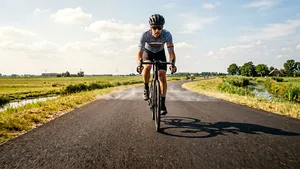 Wielrenner op de racefiets rijdt in de felle zon over zinderend heet asfalt met trillende lucht boven de weg tijdens een hittegolf.