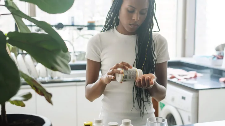 African American woman taking vitamins and supplements at home i