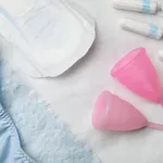 Woman's panties, menstrual pad, cups and tampons on white fabric, flat lay