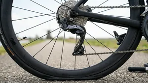 Een achter-kwart opname van een zwarte carbon racefiets (Trek Domane) op een Nederlands polderpad. De Continental Grand Prix achterband is lek en doorgezakt op het asfalt. De Shimano Ultegra derailleur en cassette zijn scherp in beeld.