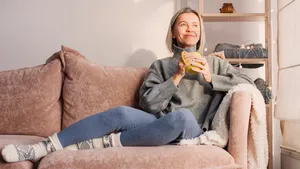 Een gelukkige, dromerige vrouw van middelbare leeftijd zit op de bank in de woonkamer met een kopje thee of koffie tijdens Dry January.