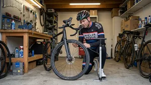 Een fietser in fietskleding kijkt met een peinzende blik naar de zachte voorband van zijn gravelbike in een garage, met een fietspomp in zijn hand.