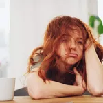 Red-haired girl sitting at table with boring face