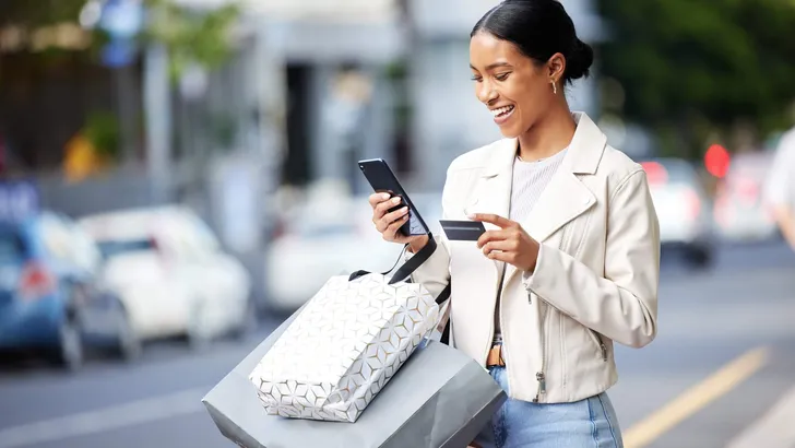 Happy woman with her phone, credit card and bag after shopping in the city. Young latin female carrying bags, spending money, looking for sales and enjoying online eCommerce store sale with a smile