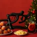 Feestelijke kerst-still met een zwarte racefiets op de achtergrond, een kerstboom met lichtjes, een donkere wijnfles, een glas glühwein met sinaasappelschijf en twee bordjes met oliebollen en kaas op een rode tafel tegen een rode achtergrond.